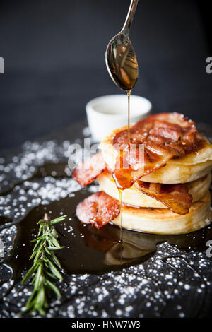 Frühstück-Speck-Fladen mit Ahornsirup Gießen aus Löffel auf Schiefer Stockfoto