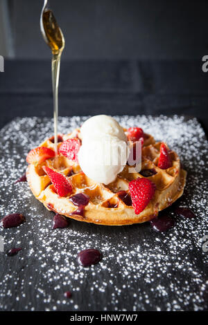 Löffel Gießen Ahorn Sirup über Erdbeeren und Eis Waffel auf Schiefer Stockfoto