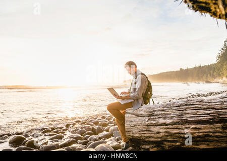 Mann, sitzend mit Laptop am Strand von Juan de Fuca Provincial Park, Vancouver Island, British Columbia, Kanada Stockfoto