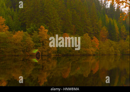 Herbstliche Bäume und Bootshaus spiegelt sich in den stillen Wassern des Loch Ard, in der Nähe von Aberfoyle, Stirlingshire, Schottland. Stockfoto