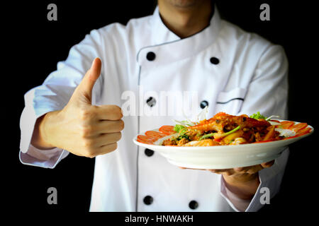 Koch mit Stolz präsentiert Curry Krabben mit Kokosnuss und zeigt Daumen hoch Stockfoto