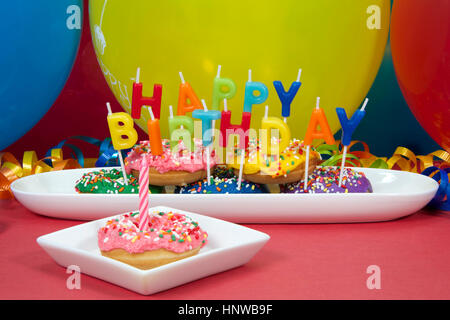 Miniatur donut Kuchen zum ersten Geburtstag. Multicolor Donuts auf weiße Platte mit Happy Birthday Kerzen. Ein rosa matt Donut Cupcake auf Platte Stockfoto