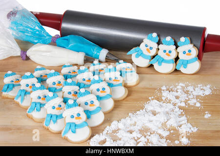 Schneemänner sugar Cookies auf einem Holztisch mit blauen und weißen Royal icing in Dekoration Taschen mit Nudelholz im Hintergrund Stockfoto