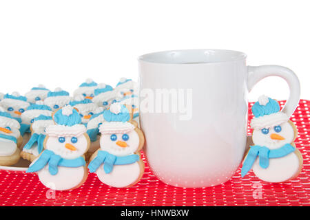 Schneemann-Butterkekse mit königlicher Zuckerglasur Zuckerguss Schals und Mützen sitzt auf einem weißen Teller auf roten Stoff Tischset mit Tasse Kaffee. Drei cookies Stockfoto