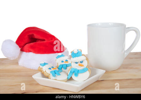 Drei Schneemänner sugar Cookies mit royal Icing frosting, Schals und Hüte auf eine quadratische weiße Platte auf Holz Leuchttisch neben Kaffee und Miniatur Stockfoto