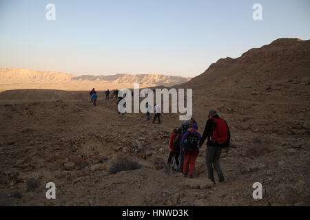 Eine Gruppe von Senioren Wanderer Fuß in Makhtesh Ramon bei Sonnenaufgang, die Berge Ferne leuchten durch die aufgehende Sonne scheint aus dem Osten. Negev, Israel. Stockfoto