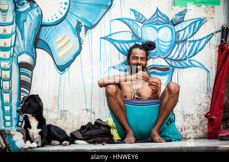 Rishikesh, Indien - 22. September 2014: Junge Pilger mit Hund sitzt in der Nähe der Wand gemalt mit Straßenkunst in Rishikesh, Indien. Stockfoto