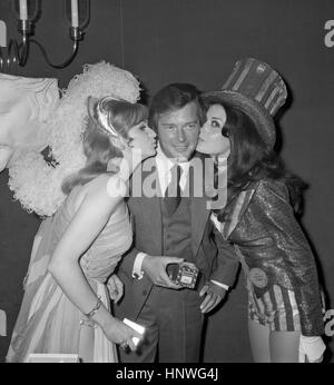Roger Moore erhält Küsse von Miss UK Marilyn Ann Ward (l) und Miss USA Brucene Smith an der Vielzahl Club of Great Britain-Mittagessen im Savoy Hotel in London. Stockfoto