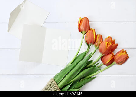 Overhead Schuss eine leere Karte und einen Strauß Tulpen über einer weißen Holz Tischplatte. Flache Laien Draufsicht Stil. Stockfoto