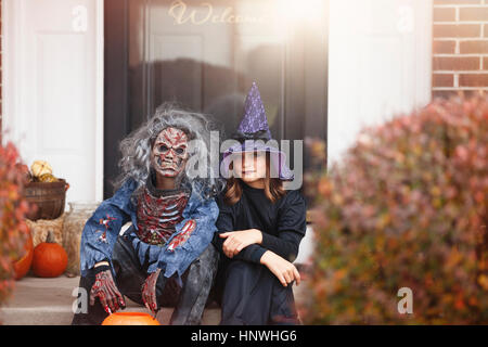 Freunde, die verkleidet als Hexe und Zombie, sitzt auf vorderen Schritt von zu Hause Stockfoto