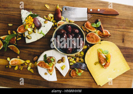 Vielfalt-Käseplatte mit Feigen, Oliven, Pistazien, Hackmesser auf Schneidbrett aus Holz Stockfoto
