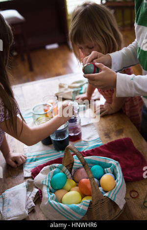 Junge und zwei Schwestern färben Ostereier am Tisch Stockfoto