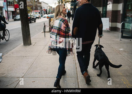 Junges Paar walking Hund entlang der Straße, Rückansicht Stockfoto