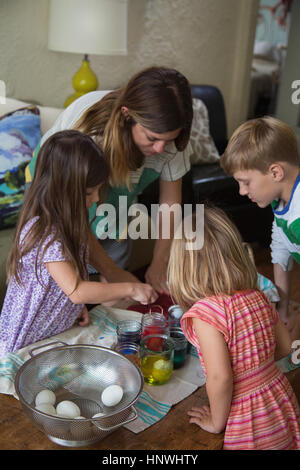 Mutter und drei Kinder färben Ostereier am Tisch Stockfoto