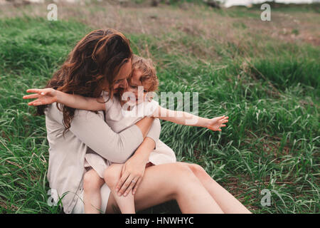 Mädchen sitzen auf Mutters Schoß auf windigen Feld Stockfoto