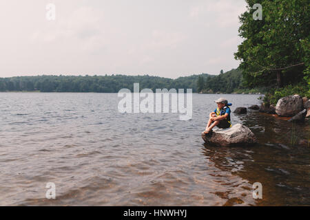 Junge sitzt auf Felsen am Rande eines Sees Stockfoto