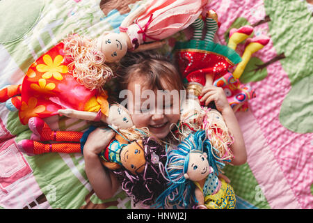 Mädchen auf Bett umgeben von Stoffpuppen Stockfoto