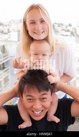 Porträt von Eltern mit Baby Sohn auf Schultern vor Fenster Stockfoto