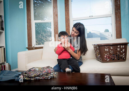 Männliche Kleinkind auf Mutters Schoß auf Sofa eine Erdbeere essen Stockfoto