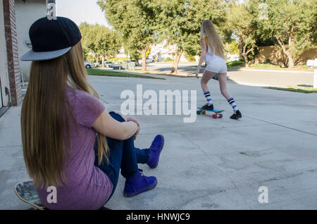 Teenager-Mädchen beobachten Schwester Skateboarden auf Bürgersteig Stockfoto