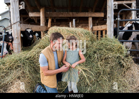 Vater und Tochter neben Kuhstall, Tochter hält Heu Stockfoto