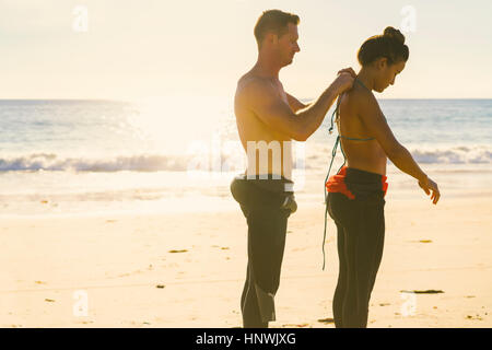 Mann hilft Freundin anziehen Neoprenanzug in Newport Beach, Kalifornien, USA Stockfoto