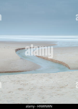 S-Kurve eines Streams wie es fließt über den goldenen Sand des Druridge Bay in die Nordsee, Northumberland in der blauen Stunde Stockfoto