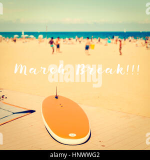 Text März brechen auf ein unscharfes Bild von einem Strand mit einem Surfbrett in den Vordergrund und unkenntlich Menschen spielen Beach-Soccer und andere Leute su Stockfoto