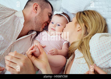 Mama und Papa küssen ihr Baby auf dem Bett liegend Stockfoto