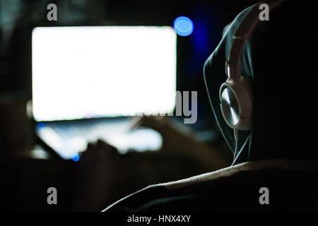 Mann-Hacker in Kapuze und Kopfhörer am Laptop im Dunkeln arbeiten Stockfoto