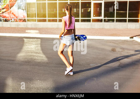 Junge Frau zu Fuß entlang der Straße, mit Skateboard, Rückansicht Stockfoto