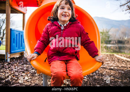 Junge sitzt auf orange Rutschbahn Stockfoto