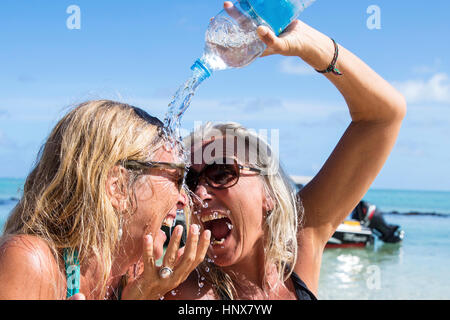 Reife weibliche Touristen gießen Wasser über Freund am Strand, Insel La Réunion Stockfoto