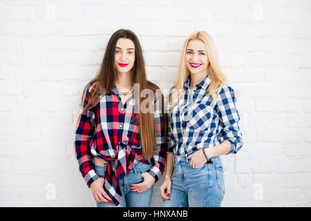 Freundinnen in karierten Hemden und Jeans stehen zusammen auf der weißen Wand Hintergrund Stockfoto