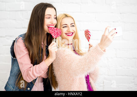 Stilvolle Freundinnen machen Selfie Foto mit roten Bonbons auf der weißen Wand-Hintergrund Stockfoto