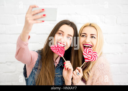 Stilvolle Freundinnen machen Selfie Foto mit roten Bonbons auf der weißen Wand-Hintergrund Stockfoto