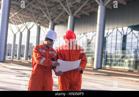 glückliches Team von jungen Ingenieuren ein Bauprojekt besprechen. Der Verschleiß Overalls und Helme. Moderne Business-Hintergrund Stockfoto