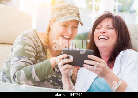 Zwei Freundinnen lachen während der Verwendung einer Smartphones auf der Terrasse. Stockfoto