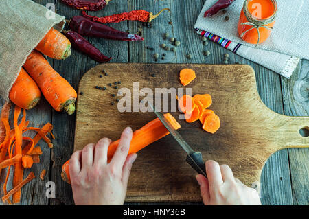 Prozess der schneiden Scheiben frische Karotten auf ein Schneidebrett, zwei menschliche Hände geschnitten ein altes Messer Gemüse Stockfoto