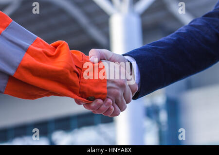 Geschäftsmann Handshaking mit Arbeiter. Handschlag von Anzug und Boilersuit. Moderne Business-Hintergrund Stockfoto