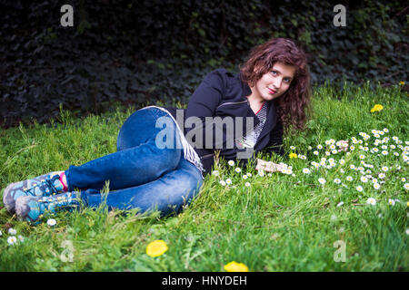 Profilbildnis des jungen Mädchens auf einem Bett von White Daisy Kamille Wildblumen und Löwenzahn lächelnd und duftenden Gras liegend Stockfoto