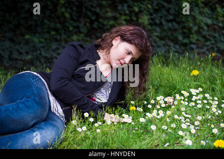 Profilbildnis des jungen Mädchens auf einem Bett von White Daisy Kamille Wildblumen und Löwenzahn lächelnd und duftenden Gras liegend Stockfoto