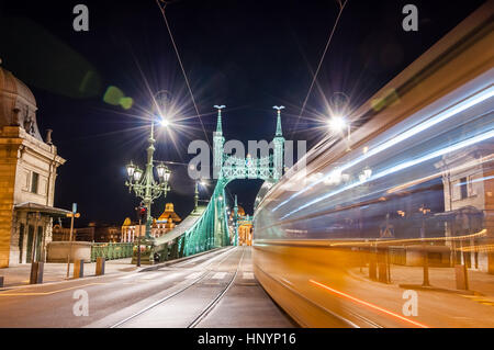 Nachtansicht der Straßenbahn auf Liberty Bridge oder Freiheitsbrücke mit Lens-Flares in Budapest, Ungarn. Stockfoto