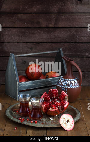 Reife Granatapfel-Frucht mit Granatapfelsaft auf Kupfer Platte und Frucht-Box und Krug auf Vintage Holztisch. Stockfoto