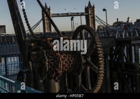 alte rostige Teile der Küsten Kran an den Ufern des Flusses in London, Zahnräder und Ketten, im Hintergrund die berühmte Tower Bridge, toller Ausblick Stockfoto