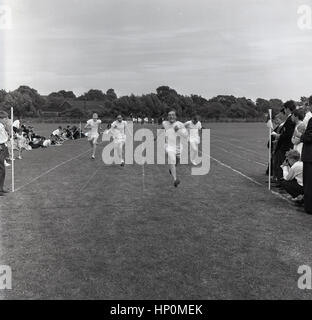 1960, historische, vier bestimmt Schuljungen, die an einem Sprint außerhalb laufende Rennen auf dem Spielfeld, England, UK. Stockfoto