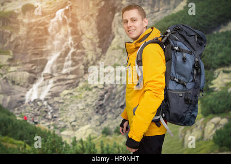 Wanderer-Mann mit Rucksack Stand am Wasserfall Stockfoto