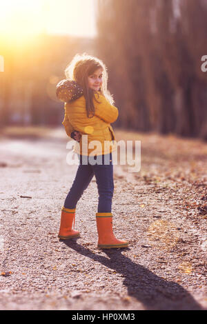 Wunderschönes kleines Mädchen in orange Jacke und Gummistiefel Stockfoto