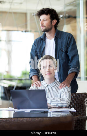 Mann massiert Frau Schultern, weil sie auf Laptop-Computer arbeitet Stockfoto