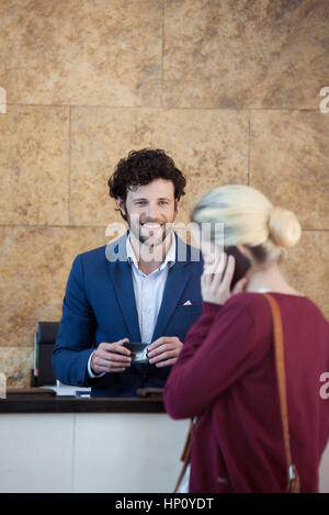 Freundliche Angestellte an der Rezeption warten gerne Kunde auf Handy Stockfoto